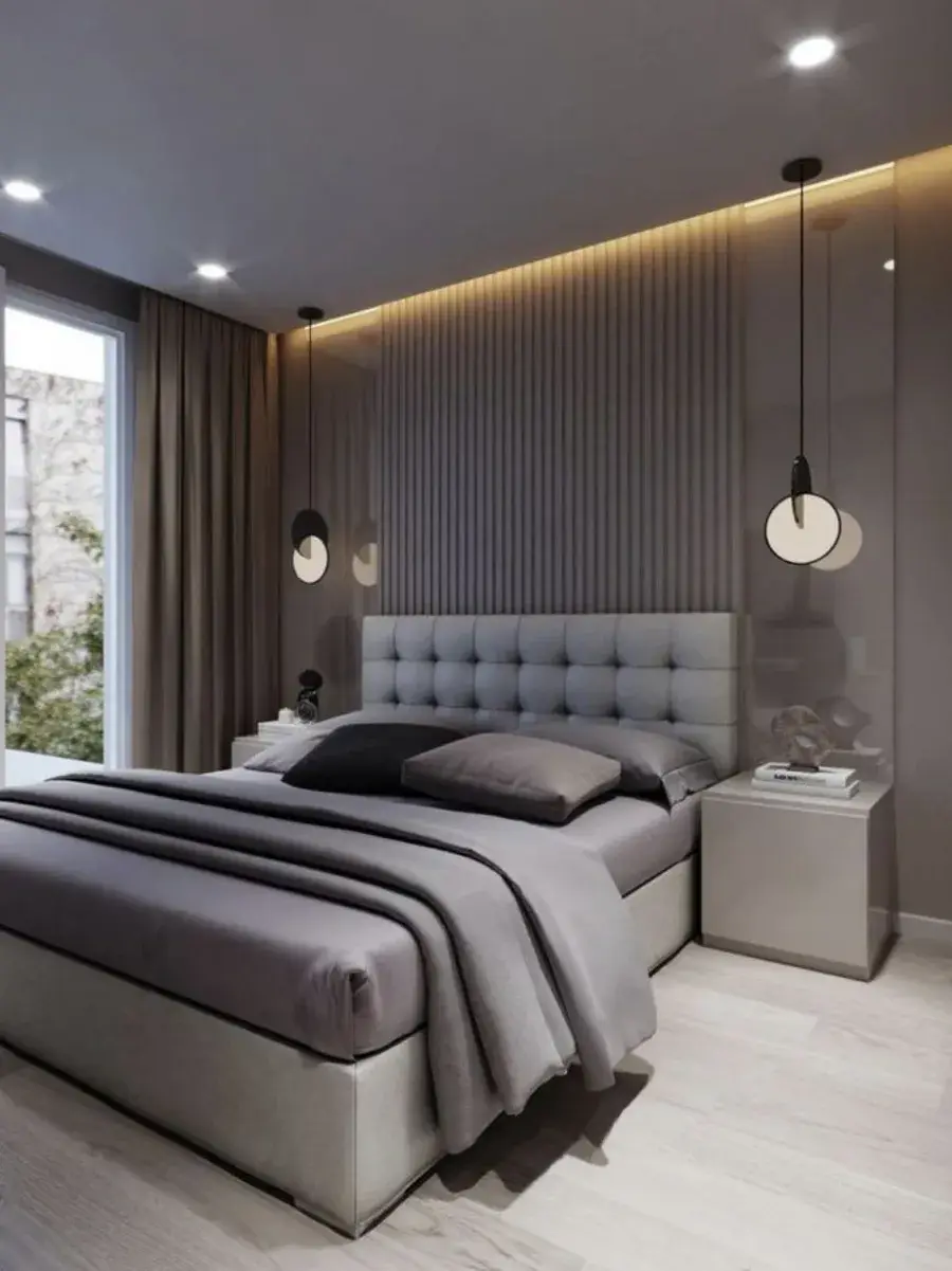 A made bed with grey linens and a tufted headboard in a bedroom with warm cove lighting and slatted walls