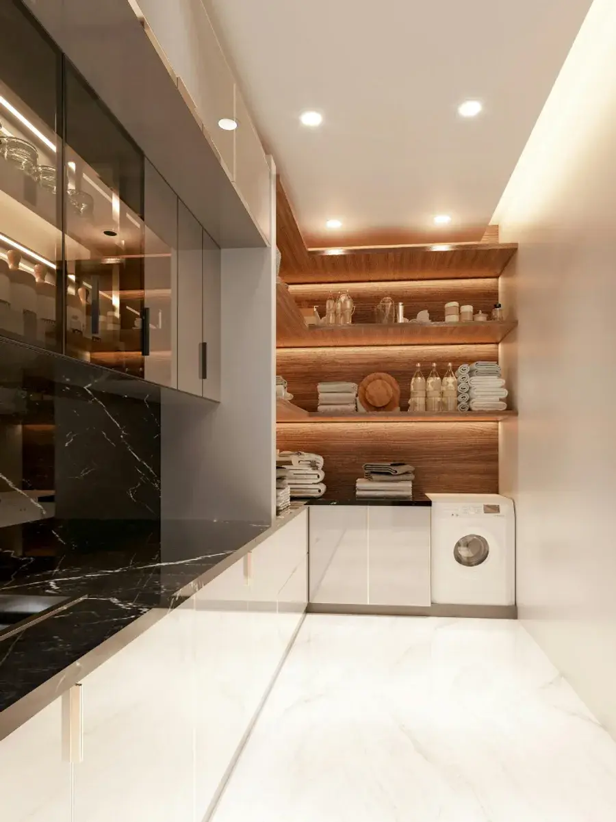 A laundry room with a washing machine, towels stacked on lit wooden shelves and a marble-look floor